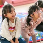 Two young girls laughing and smiling during a fun lesson at Rocket English School・ロケットイングリッシュスクールでの楽しいレッスン中、2人の少女が笑みを浮かべている