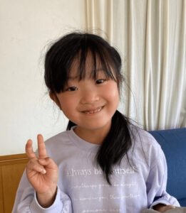 A young girl smiling and making the peace sign with her fingers ・笑顔で指でピースサインをする少女