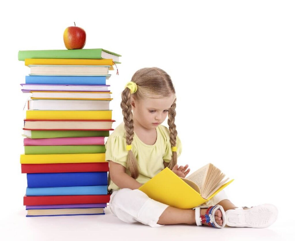 Girl reading a book next to a large pile of books