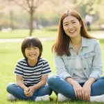 晴れた公園で母親と息子が笑顔で座っている様子。