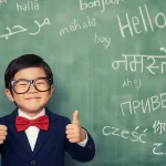 A boy stands smiling in front of a blackboard filled with different words for "Hello"